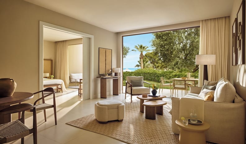 One Bedroom Bungalow Suite Private Pool Garden View living area with neutral decor, organic textures, and large windows overlooking a sunny resort landscape at Sani Club by Kenwood Travel