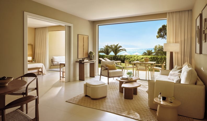Two Bedroom Bungalow Suite Private Garden Sea View beachfront hotel suite living room with neutral, minimalist decor, open layout leading to a bedroom, and large glass windows overlooking a sunny ocean view with palm trees at Sani Club by Kenwood Travel