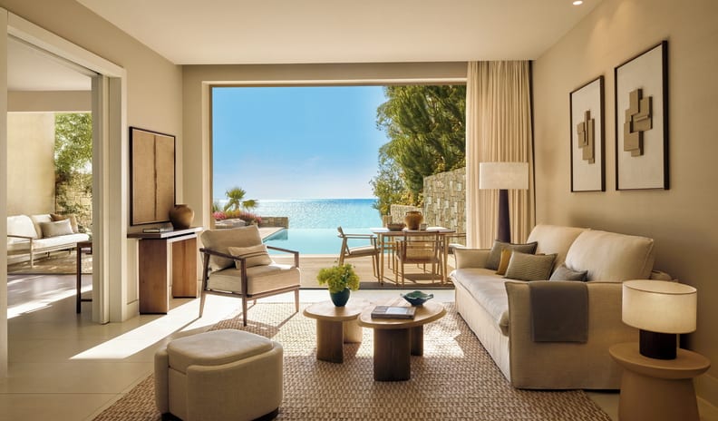 Two Bedroom Bungalow Suite PrIvate Pool Beach Front Modern Mediterranean living room with neutral linen sofas, wooden accent tables, and a large open doorway leading to a sunny terrace at Sani Club by Kenwood Travel