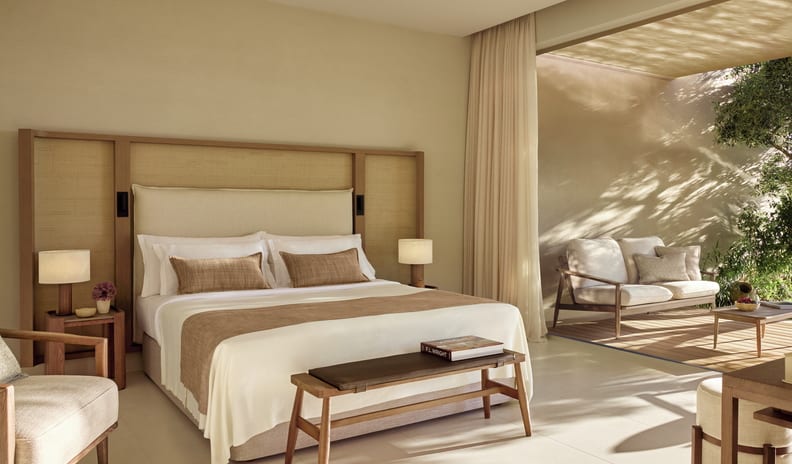 Two Bedroom Bungalow Suite Private Pool Front Sea Viewbedroom featuring a large bed with a tall woven headboard, cream linens, a wooden end-of-bed bench, and open doors leading to a private shaded patio at Sani Club by Kenwood Travel
