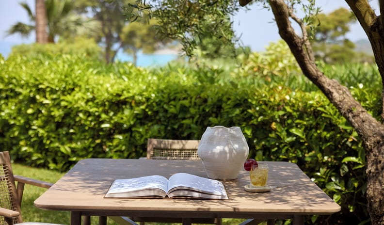 One Bedroom Bungalow Suite Private Pool Garden View garden terrace table with an open book, vase, and drink, surrounded by tropical greenery and palm trees at Sani Club by Kenwood Travel