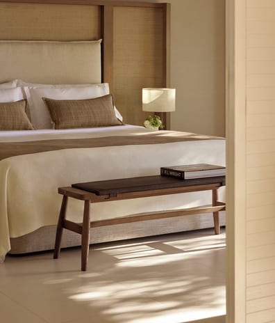 Two Bedroom Bungalow Suite Private Garden Sea View Luxury resort king bed featuring crisp white linens, earth-toned decorative pillows, a large woven headboard, and a wooden end-of-bed bench with a leather cushion at Sani Club by Kenwood Travel