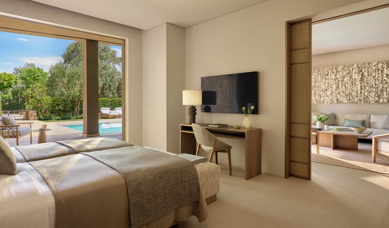 Three Bedroom Grand Residence Private Pool Garden View Bright and airy villa bedroom featuring natural linen bedding, a TV desk setup, and direct outdoor access to a sunlit pool deck at Sani Asterias by Kenwood Travel
