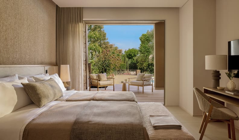 Three Bedroom Grand Residence Private Pool Garden View two twin beds with neutral linens, a textured accent wall, a writing desk, and open sliding doors leading to a private garden patio at Sani Asterias by Kenwood Travel