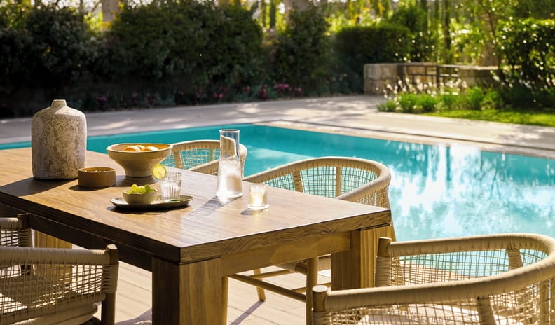 Three Bedroom Grand Residence Private Pool Garden View unlit al fresco dining space at a premium villa, showcasing a beautifully styled wooden table next to a private swimming pool at Sani Asterias by Kenwood Travel