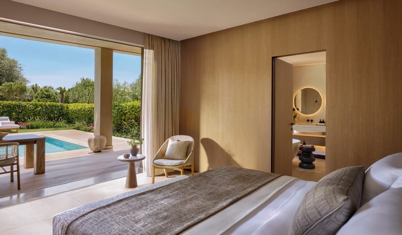 Three Bedroom Grand Residence Private Pool Garden View bedroom with an en-suite bathroom, indoor lounge seating, and direct floor-to-ceiling door access to a private swimming pool and sun terrace at Sani Asterias by Kenwood Travel