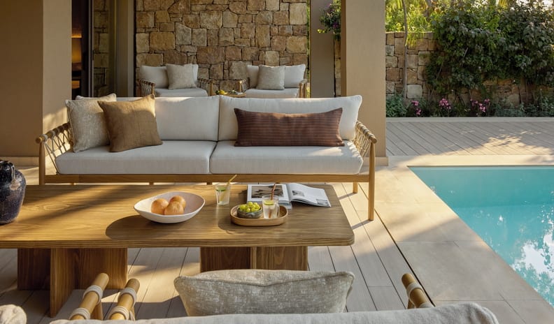 Three Bedroom Villa Pr. Pool Garden View poolside terrace of a luxury hotel villa, featuring a stylish outdoor lounge area, sunlit timber decking, a crystal-clear swimming pool, and traditional Mediterranean stone masonry at Sani Asterias by Kenwood Travel