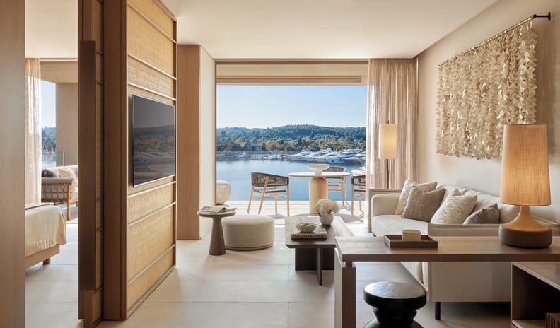 One Bedroom Residence Grand Balcony Marina Front living room featuring a modern beige sofa, open partition wall with a flat-screen TV, and a glass balcony looking out at a marina at Sani Asterias by Kenwood Travel