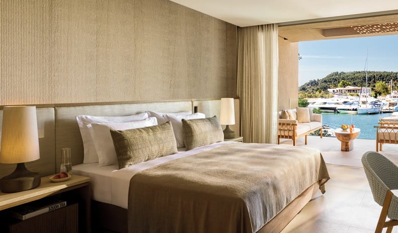One Bedroom Residence Grand Balcony Marina Front Mediterranean bedroom design featuring a ribbed accent wall, neutral linen bedding, and seamless indoor-outdoor transition to a patio at Sani Asterias by Kenwood Travel