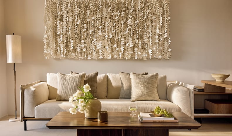 One Bedroom Residence Private Garden Marina Front living room design showcasing a neutral color palette, a minimalist floor lamp, wooden furniture, and a large multi-layered textured fabric wall installation above the couchat Sani Asterias by Kenwood Travel