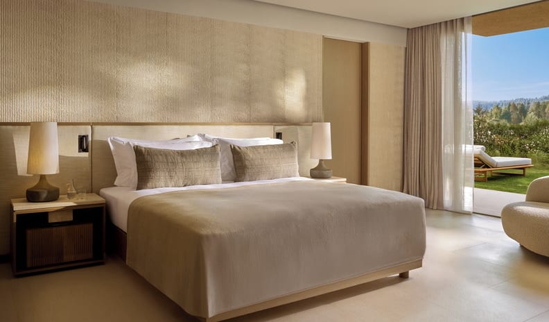 One Bedroom Residence Private Garden Marina Front bedroom featuring a large bed with taupe linens, elegant bedside lamps, and seamless indoor-outdoor transition to a private garden at Sani Asterias by Kenwood Travel