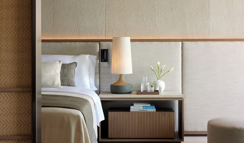 One Bedroom Residence Private Garden Marina Front bedroom vignette showing a partial view of a bed with neutral linens, an upholstered headboard, and a carefully styled nightstand with books and a water carafe at Sani Asterias by Kenwood Travel