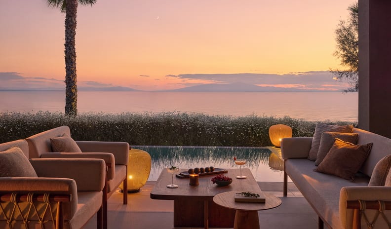 Two Bedroom Signature Residence Pr. Pool Beach Front private beachfront villa terrace arranged with premium outdoor furniture, refreshments, and a glowing sunset over distant mountains across the sea at Sani Asterias by Kenwood Travel