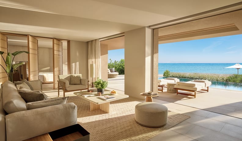 Two Bedroom Signature Residence Pr. Pool Beach neutral sofas, a woven area rug, and expansive pocket doors opening up to a sunny Mediterranean sea terrace at Sani Asterias by Kenwood Travel