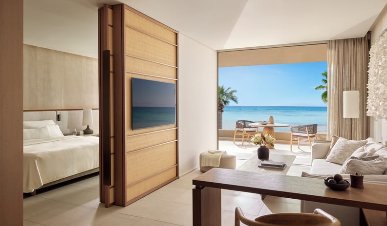 One Bedroom Residence Grand Balcony Beach Front SV living area, flat-screen TV on a woven wood partition, and a scenic ocean-view balcony at Sani Asterias by Kenwood Travel