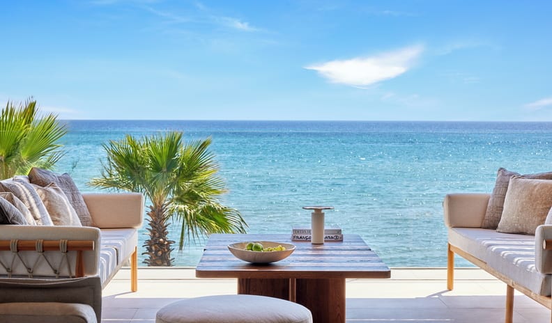 One Bedroom Residence Grand Balcony Beach Front SV outdoor sofas and a wooden coffee table overlooking a vibrant blue ocean at Sani Asterias by Kenwood Travel