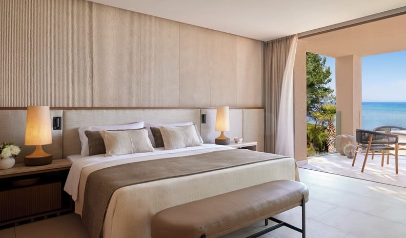 One Bedroom Residence Grand Balcony Beach Front SV with a king-size bed, beige decor, and an open balcony overlooking the ocean at Sani Asterias by Kenwood Travel