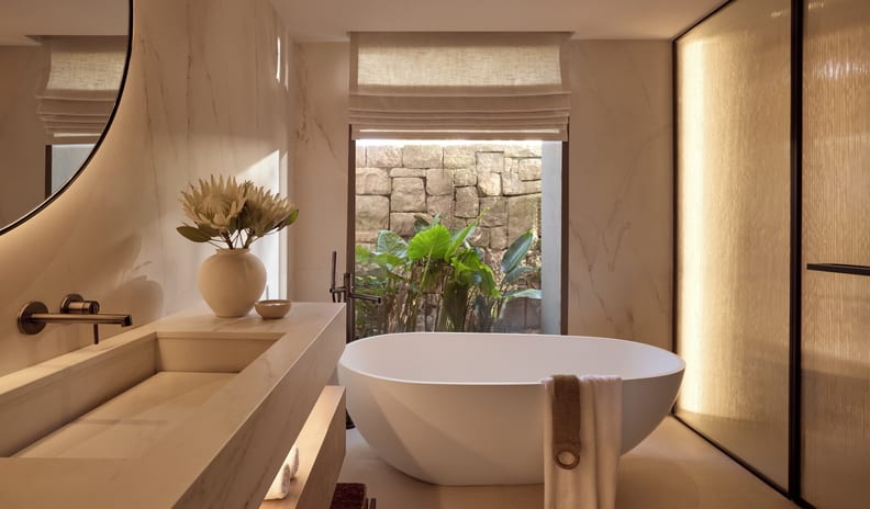 One Bedroom Residence Private Garden Beach Front SV bathroom featuring a modern freestanding soaking tub, marble floating vanity, and a window looking out onto tropical greenery at Sani Asterias by Kenwood Travel