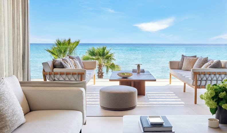 Two Bedroom Grand Residence Balcony Beach Front SV Luxury hotel suite bedroom with a king-sized bed, warm neutral decor, and a large open balcony featuring an outdoor dining table overlooking the blue ocean at Sani Asterias by Kenwood Travel