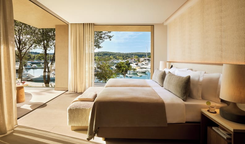 Two Bedroom Residence Balcony Marina Front bedroom with a large open window overlooking a sunny marina filled with yachts and boats at Sani Asterias by Kenwood Travel