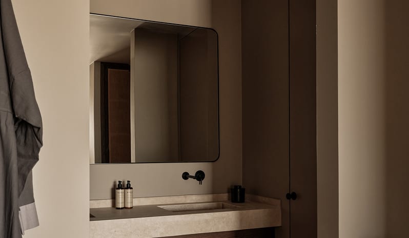 Two Bedroom Suite with Private Pool wabi-sabi bathroom design with earth-toned plaster walls, a custom stone washbasin counter, a woven floor basket, and minimalist matte black hardware at OKU Bodrum by Kenwood Travel