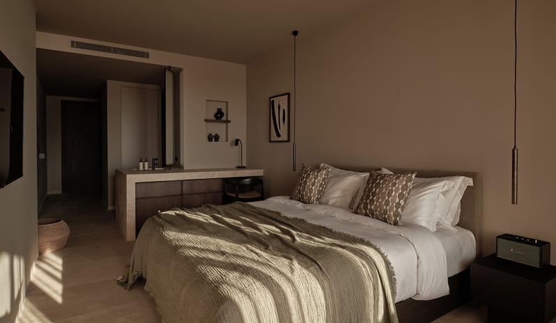 Classic Room with Shared Pool earthy neutral tones, a bed with an olive green textured throw, patterned pillows, sleek hanging pendant lights, and warm natural sunlight at OKU Bodrum by Kenwood Travel