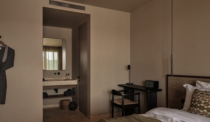 Junior Suite wabi-sabi bedroom interior featuring a floating stone sink vanity, matte black fixtures, and a sleek dark wood writing desk at OKU Bodrum by Kenwood Travel