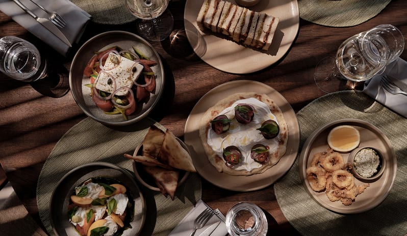 To Kima Mediterranean lunch spread with various small plates, flatbreads, seafood, and wine on a dark wooden table at OKU Bodrum by Kenwood Travel