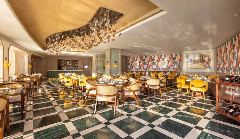 Riviera interior design showcasing checkered marble flooring, cane-back chairs, vibrant geometric wallpaper, and custom lighting at Rixos Radamis Sharm El Sheikh by Kenwood Travel