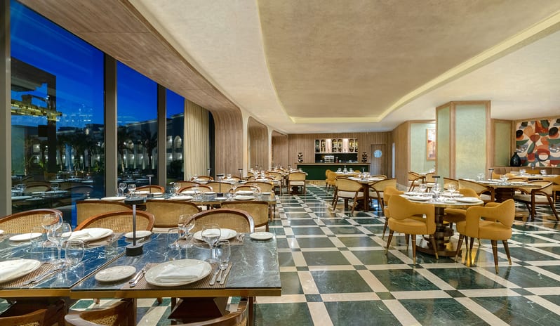 Riviera dining room showcasing green and white checkered marble floors, cane-back chairs, a curved lit ceiling, and a green accent bar at Rixos Radamis Sharm El Sheikh by Kenwood Travel