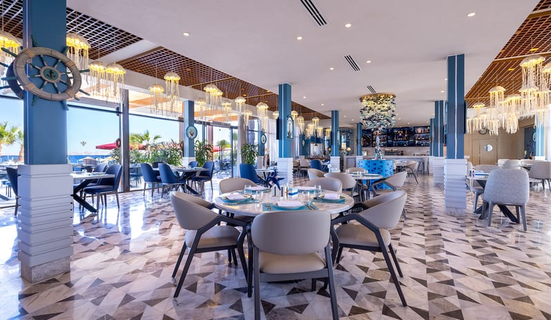 Salt dining room featuring unique jellyfish pendant lights, blue pillars, a decorative ship wheel, and geometric tiled floors at Rixos Radamis Sharm El Sheikh by Kenwood Travel