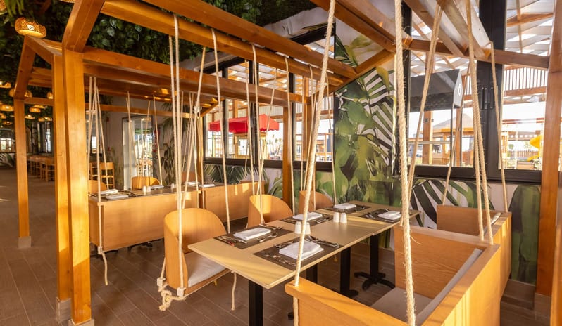 Kids Restaurant Wooden dining tables with indoor hanging swing chairs and tropical leaf wallpaper in a modern restaurant at Rixos Radamis Sharm El Sheikh by Kenwood Travel