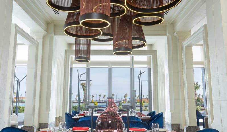 T-Bone Fine dining tables set with royal blue velvet chairs and distinctive overhead light fixtures at Rixos Radamis Sharm El Sheikh by Kenwood Travel