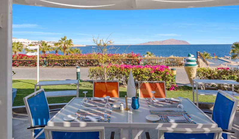 Viva Mar Al fresco resort dining table with ocean views, pink bougainvillea flowers, and a decorative ice cream cone sculpture at Savoy Sharm El Sheikh by Kenwood Travel
