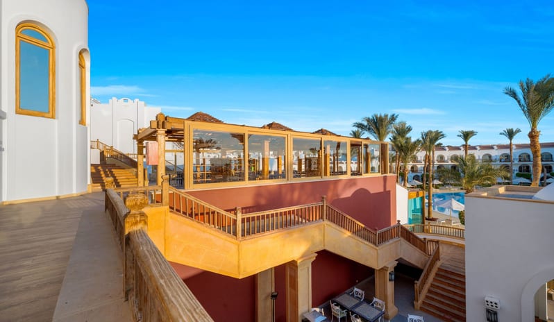 Tirana Sunlit outdoor terrace and glass-walled pavilion at a luxury resort overlooking a swimming pool and palm trees at Savoy Sharm El Sheikh by Kenwood Travel