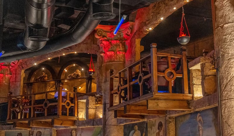Caligula Hot Rock Interior of an ancient Roman-themed restaurant featuring rustic wooden balconies, stone pillars, and dramatic red accent lighting at Savoy Sharm El Sheikh by Kenwood Travel