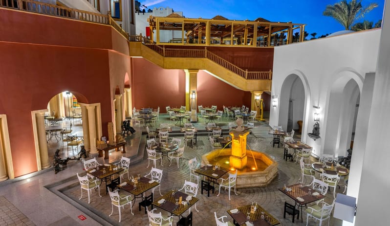 Rosmarino central fountain, white patio dining sets, and elegant architecture at dusk at Savoy Sharm El Sheikh by Kenwood Travel