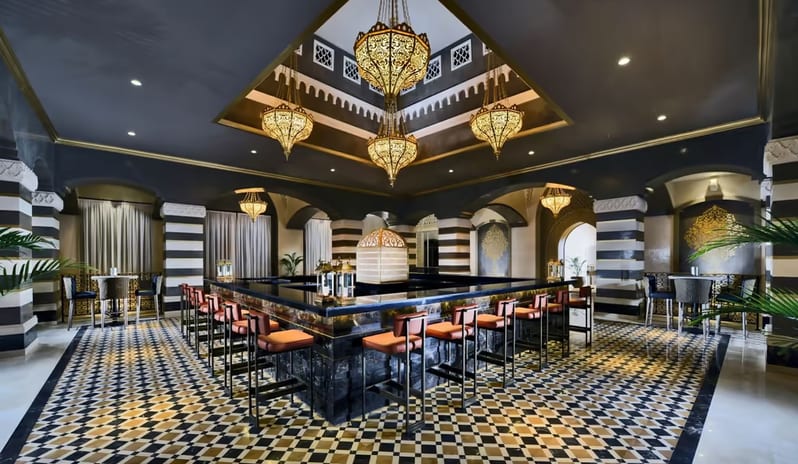 Cazar Bar square central bar, tiled floors, and ornate golden hanging chandeliers at Steigenberger Alcazar by Kenwood Travel