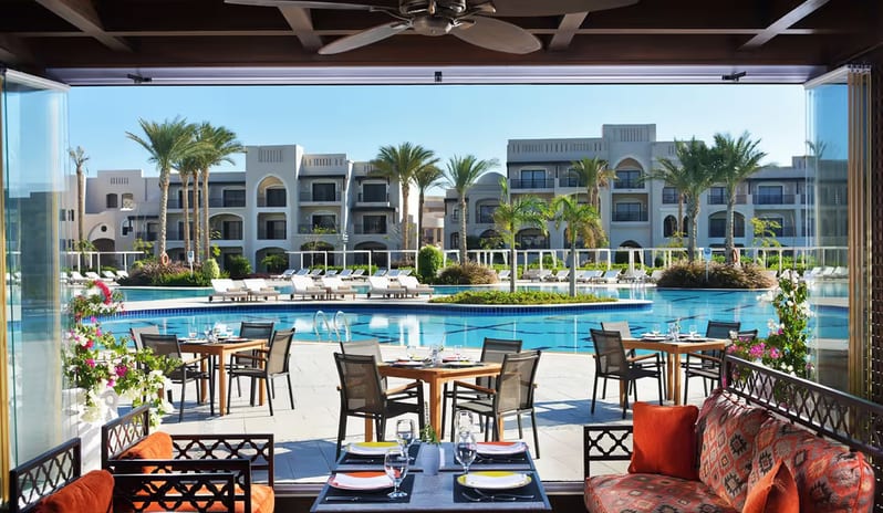 Amoura Restaurant Outdoor dining tables at Amoura Restaurant overlooking a luxury resort swimming pool and palm trees at Steigenberger Alcazar by Kenwood Travel