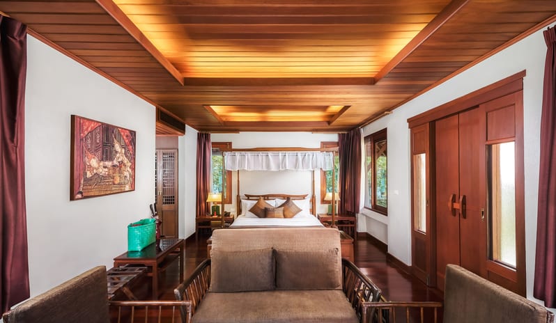 Oriental Villa polished wooden ceiling, canopy king bed, and a cozy lounge seating area at Khaolak Laguna Resort by Kenwood Travel