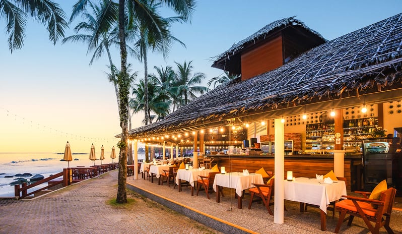 Sundowner Beachside Terrace outdoor beachfront dining tables under a thatched roof bar at sunset at Khaolak Laguna Resort by Kenwood Travel