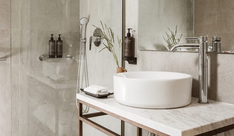 Botanica Bungalow Shaded Veranda bathroom interior design showcasing light grey wall tiles, an open-frame metal vanity with a marble countertop, and a round vessel sink at Grecotel LUXME Costa Botanica by Kenwood Travel