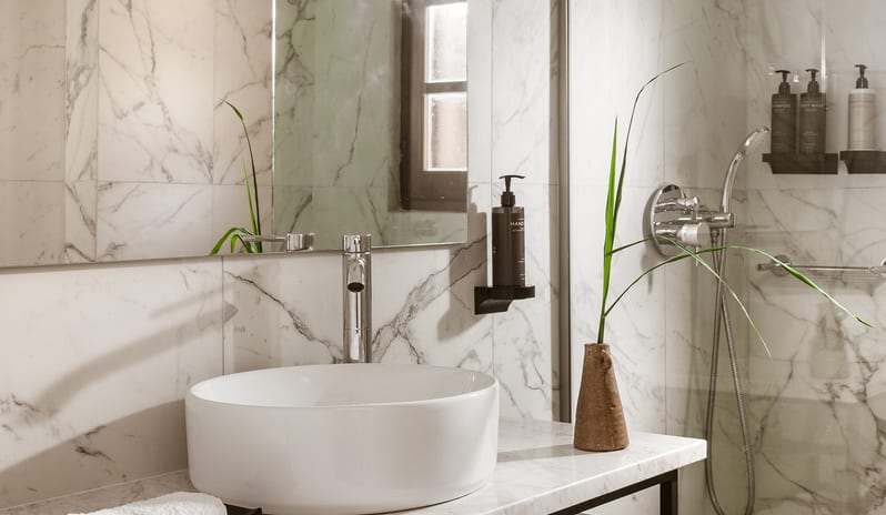 Family Interconnecting Loft Private Balcony Polished white marble tiles with grey veining installed in a contemporary bathroom alongside a chrome shower fixture and sink faucet at Grecotel LUXME Costa Botanica by Kenwood Travel