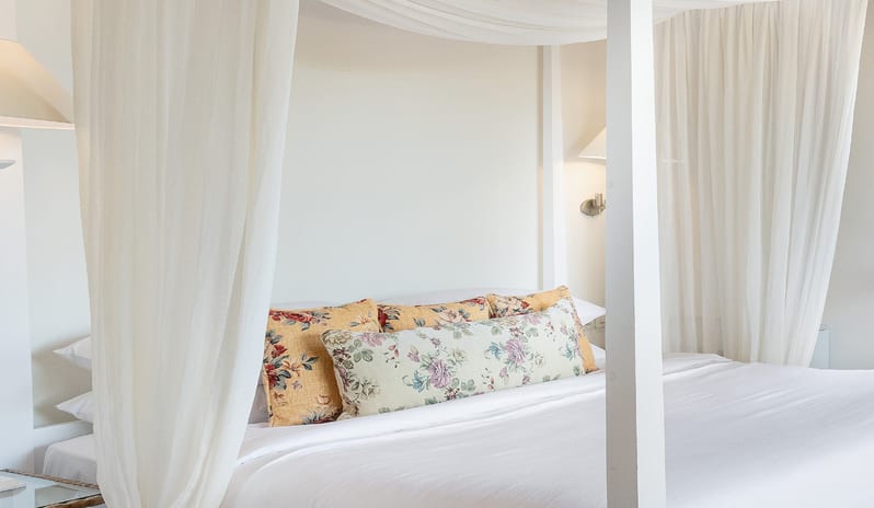 Family Interconnecting Loft Private Balcony wooden four-poster canopy bed with sheer curtains, a white comforter, and patterned lumbar pillows at Grecotel LUXME Costa Botanica by Kenwood Travel