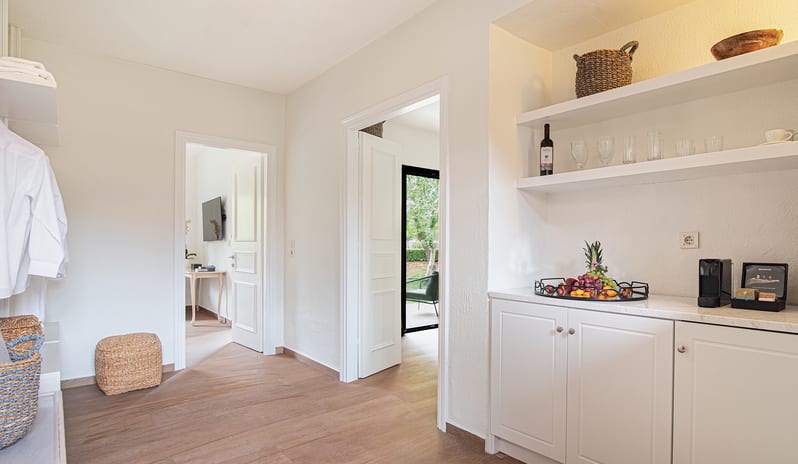 Family Summer Home Shaded Veranda & Gardens Bright luxury villa hallway layout showcasing a custom wet bar, open walk-in wardrobe shelving, wood floors, and a central doorway opening out to a sunny garden patio at Grecotel LUXME Costa Botanica by Kenwood Travel