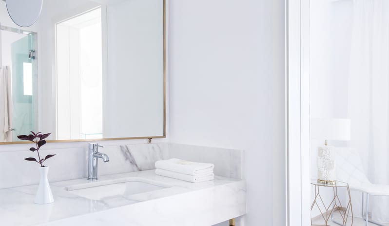 LUX ME Bungalow Poolside bathroom showing a stone vanity layout with fresh towels, a geometric side table visible in the next room, and all-white modern finishes at Grecotel LUXME Dama Dama by Kenwood Travel