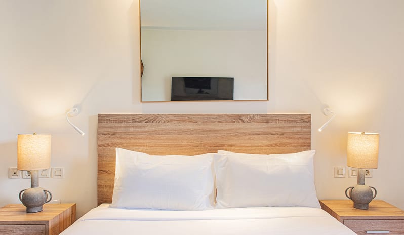 Botanica Bungalow Shaded Veranda Pair of modern ceramic table lamps emitting a warm glow on light wood nightstands flanking a bed with white linens at Grecotel LUXME Costa Botanica by Kenwood Travel