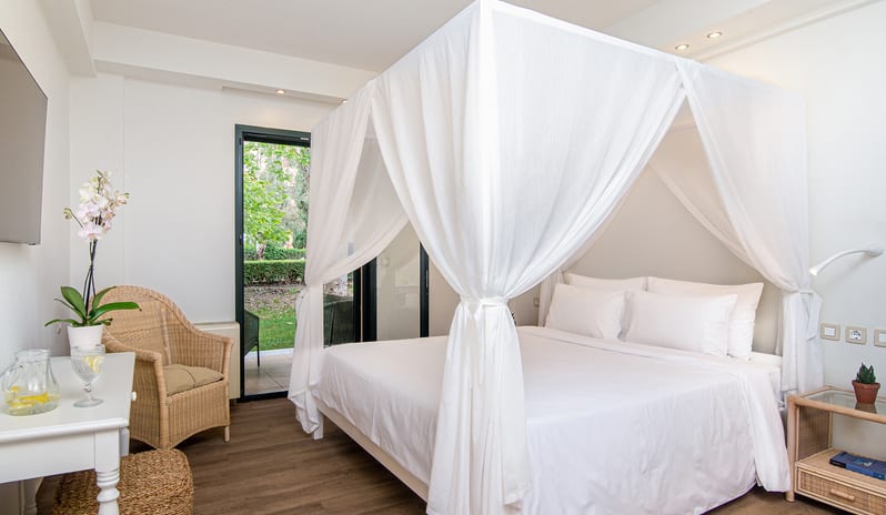 Family Interconnecting Room Shaded Veranda white-draped canopy bed, a woven seagrass ottoman, a wicker armchair, and a potted orchid on a writing desk at Grecotel LUXME Costa Botanica by Kenwood Travel