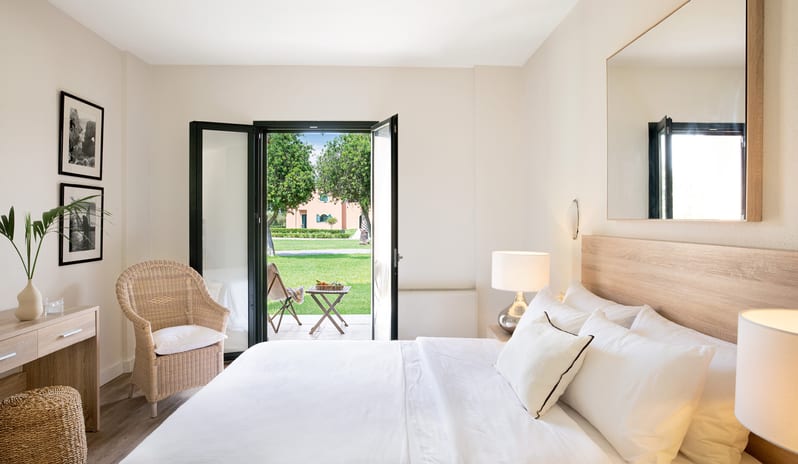 Botanica Bungalow Shaded Veranda sunlit bedroom with an open entrance leading directly to a private tiled terrace and a manicured garden layout at Grecotel LUXME Costa Botanica by Kenwood Travel