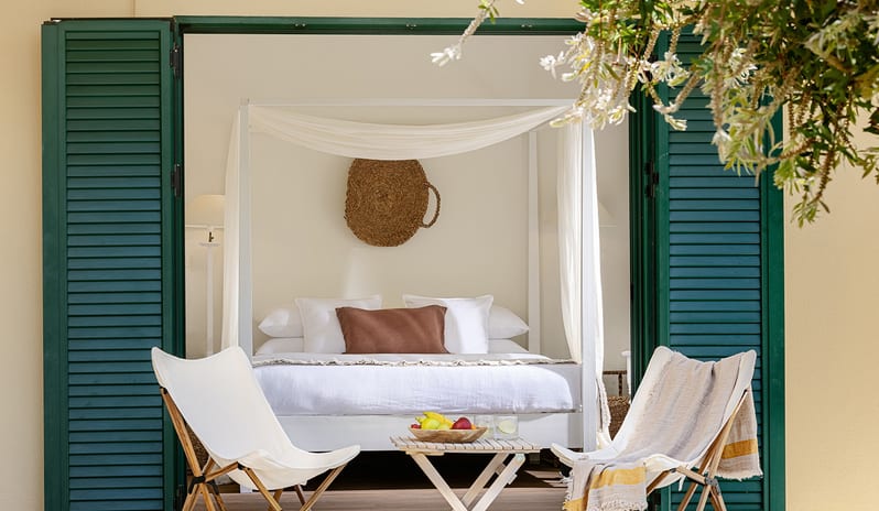 Family Interconnecting Room Shaded Veranda Private shaded veranda with outdoor lounge chairs looking into a boutique hotel family interconnecting room with a white canopy bed at Grecotel LUXME Costa Botanica by Kenwood Travel